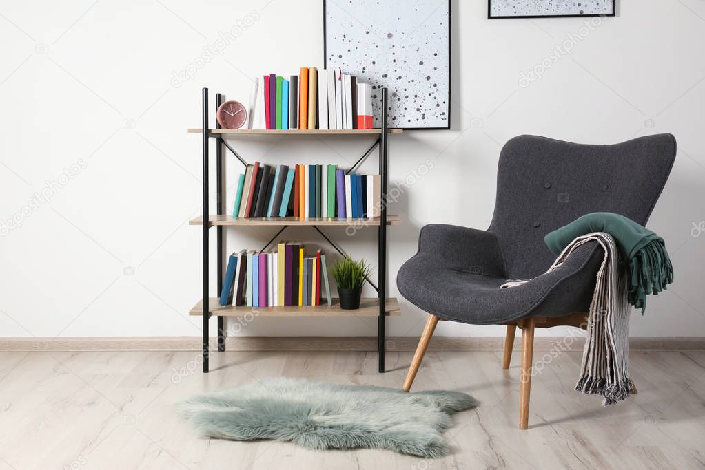 Comfortable armchair and shelving unit with different books near wall in room