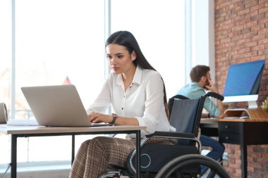 İş yerinde dizüstü bilgisayar kullanan tekerlekli sandalyedeki genç kadın
