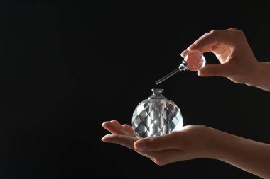 Siyah arka planda lüks parfüm şişesi tutan kadın, yakın plan. Metin için boşluk