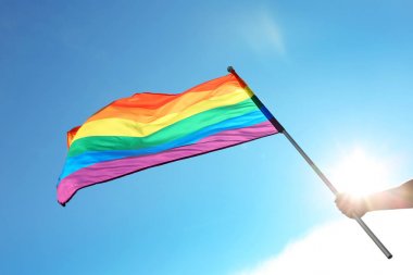 Mavi gökyüzüne karşı gökkuşağı Lgbt bayrağı tutan eşcinsel adam