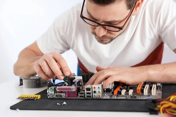 Male technician repairing motherboard at table against light background