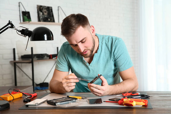 Техник по ремонту мобильного телефона за столом в мастерской
