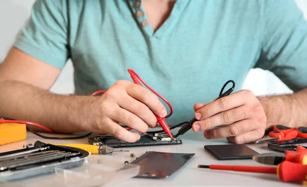 Tecnico che controlla il telefono cellulare a tavola in officina, primo piano — Foto Stock