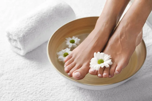 Vista de cerca de la mujer empapando sus pies en plato con agua y flores en toalla blanca, espacio para el texto. Tratamiento de spa — Foto de Stock