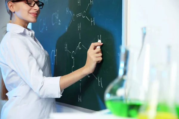 Ženský vědec, který píše chemický vzorec na chalkici v interiéru — Stock fotografie