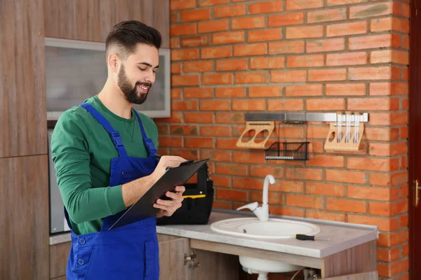 Plomero masculino con portapapeles cerca del fregadero de la cocina. Servicio de reparación —  Fotos de Stock