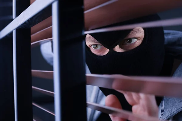 Hombre enmascarado espiando a través de persianas de ventana en el interior. Delitos penales — Foto de Stock