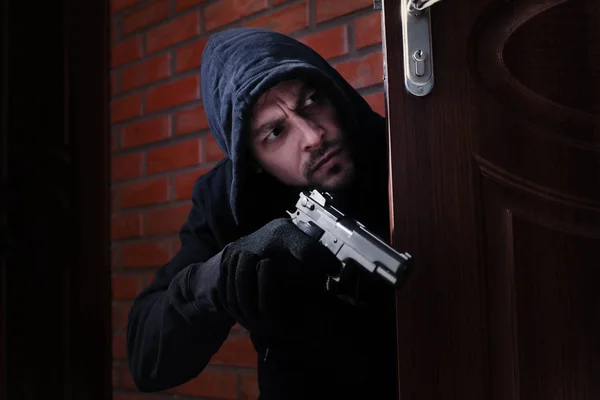 Людина з пістолетом шпигує за відкритими дверима в приміщенні. Кримінальне правопорушення — стокове фото