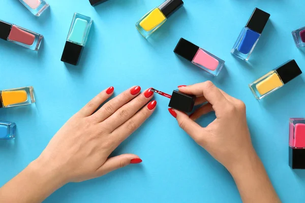 Woman applying bright nail polish on color background, top view — 스톡 사진