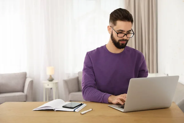 Yakışıklı genç adam ev ofisinde masada dizüstü bilgisayar ile çalışıyor — Stok fotoğraf