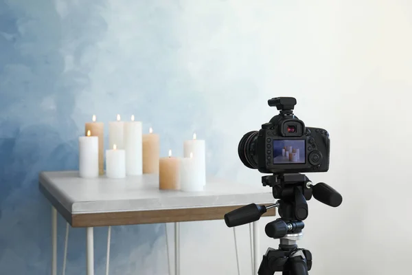 Professional camera and candles on table against color wall — Stock Photo, Image
