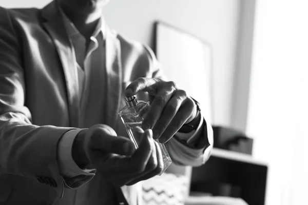 Homem aplicando perfume no pulso dentro de casa, fechar com espaço para texto. Efeito preto e branco — Fotografia de Stock