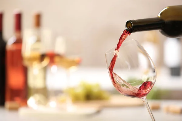 Pouring red wine from bottle into glass on blurred background. Space for text — Stock Photo, Image