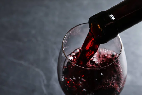 Despejar vinho tinto da garrafa em vidro sobre fundo cinza, close-up. Espaço para texto — Fotografia de Stock