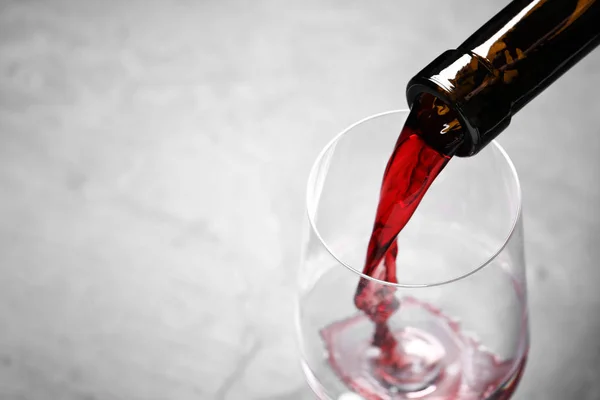 Versare il vino rosso dalla bottiglia in vetro su fondo chiaro, primo piano. Spazio per testo — Foto Stock