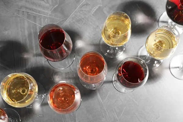 Bicchieri diversi con vino su sfondo grigio, posa piatta — Foto Stock