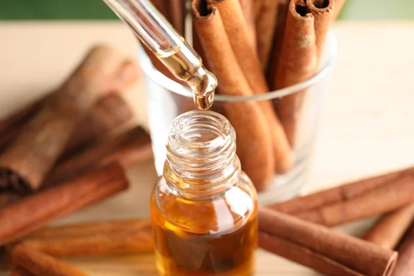 Pipeta com óleo essencial sobre garrafa e paus de canela na mesa, close-up — Fotografia de Stock