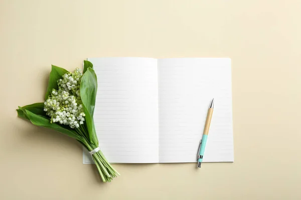 Notebook, pen and lily of the valley bouquet on color background, flat lay. Space for text — Stock Photo, Image