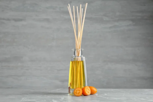Reed freshener aromático e kumquat na mesa contra fundo cinza — Fotografia de Stock