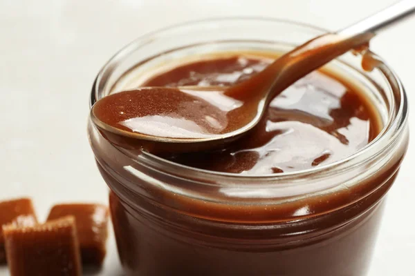 Jar with tasty caramel sauce and spoon on table, closeup Stock Image