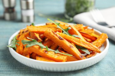 Ahşap masa üzerinde pişmiş tatlı patates dilimleri ve arugula ile Tabak, closeup