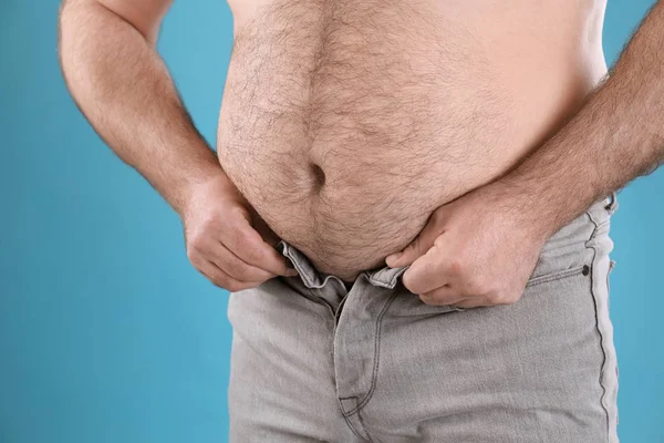 Overweight man trying to button jeans on color background, closeup