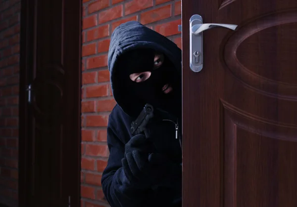 Homem mascarado com espingarda atrás da porta aberta dentro de casa. Infracção penal — Fotografia de Stock