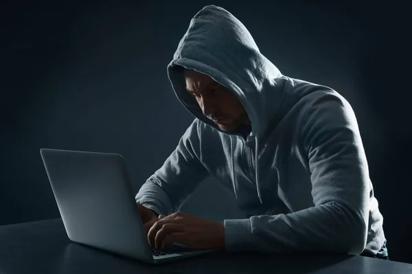 男子在黑暗的背景使用笔记本电脑在桌子上。犯罪活动 — 图库照片