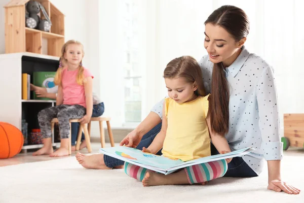 Professor de jardim de infância lendo livro para criança dentro de casa, espaço para texto. Aprendizagem e jogo — Fotografia de Stock