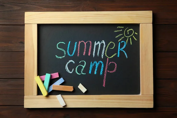 Kleine Tafel mit Text Sommerlager, Zeichnung und Kreidestäbchen auf Holzgrund, Draufsicht — Stockfoto