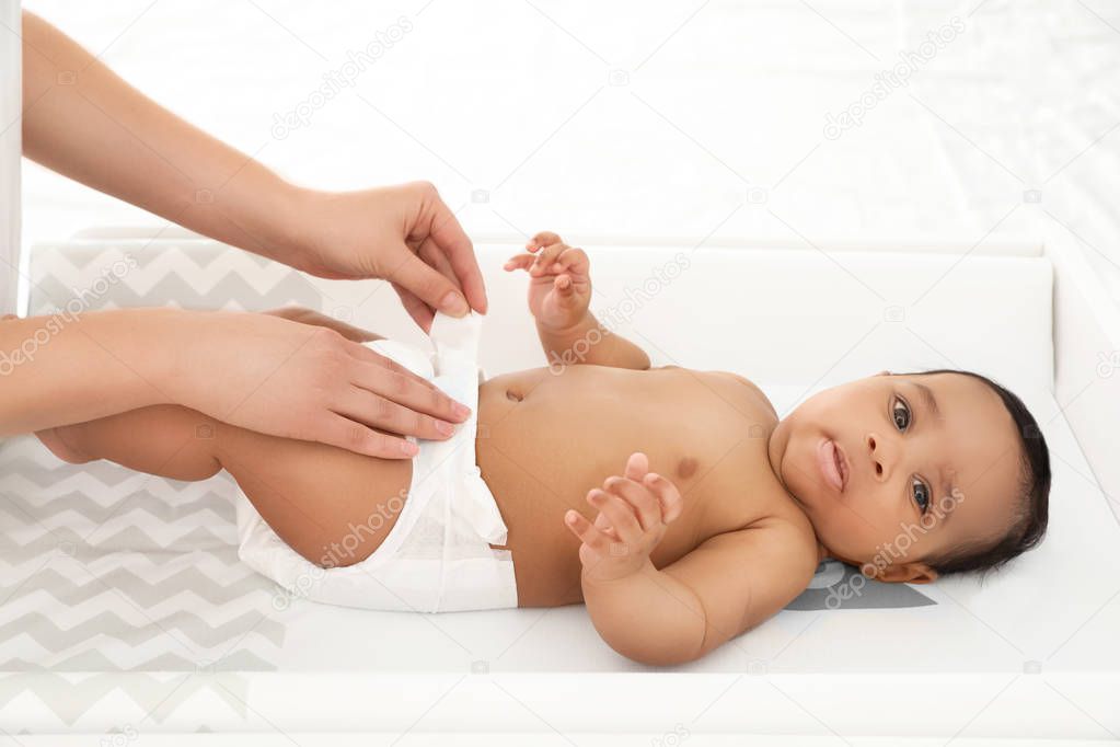 Mother changing her baby's diaper on table indoors