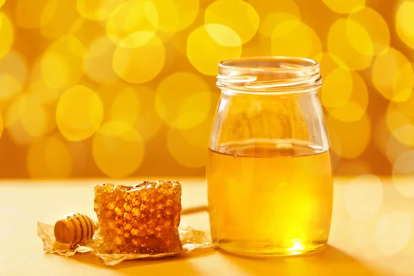 Jar with honey and fresh comb on table against blurred background — Stock Photo, Image