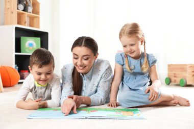 Anaokulu öğretmeni kapalı çocuklara kitap okuyor. Öğrenme ve oynama