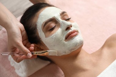 Spa salonunda kadının yüzüne beyaz maske uygulayan kozmetolojist, yakın çekim