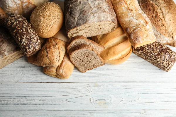 Diferentes tipos de pan fresco en la mesa de madera, la puesta plana. Espacio para texto — Foto de Stock
