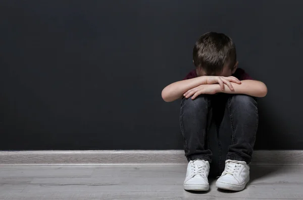 Sad little boy on floor near black wall. Space for text — Stock Photo, Image