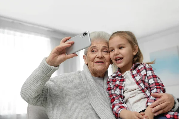 Menina bonito e sua avó tomando selfie em casa — Fotografia de Stock