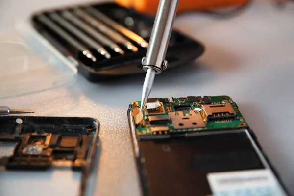 Reparación de teléfono móvil roto con soldador en la mesa, primer plano —  Fotos de Stock