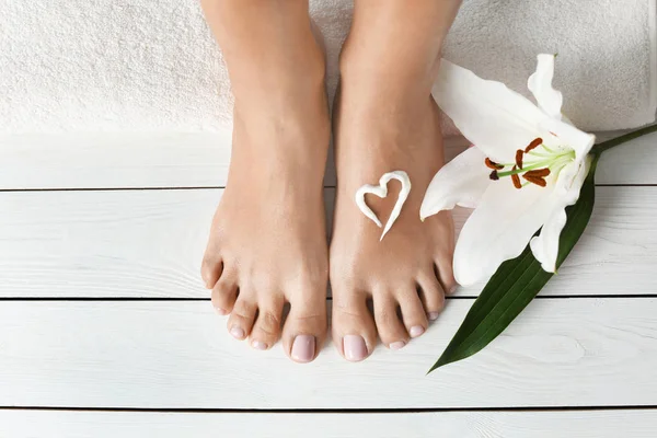 Woman with beautiful feet, cream, flower and towel on white wooden floor, closeup. Spa treatment