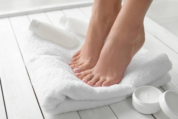 Vrouw met mooie voeten, handdoek en cosmetische producten op witte houten vloer, close-up. Kuuroord — Stockfoto