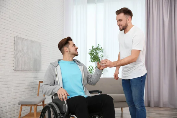 Vrijwilliger geven van glas water aan de mens in een rolstoel thuis. Hulp bij uitgeschakelde — Stockfoto