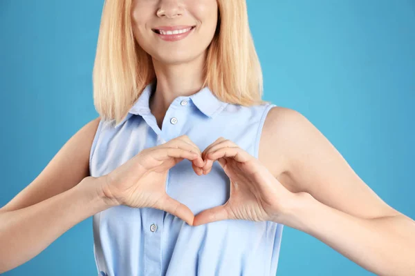 Vrouw maken van hart met haar handen op kleur achtergrond, close-up — Stockfoto
