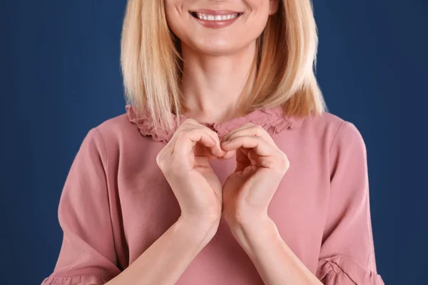 Vrouw maken van hart met haar handen op kleur achtergrond, close-up — Stockfoto