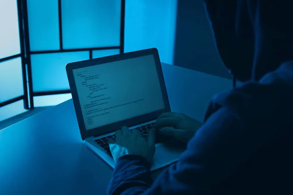 Mand, der bruger bærbar computer ved bordet i mørkt rum, tæt på. Strafferetlig forfølgelse - Stock-foto