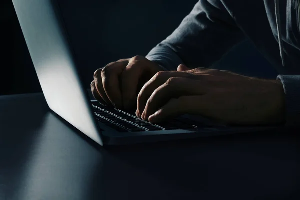 Homem usando laptop na mesa no fundo escuro, close-up. Actividade criminosa — Fotografia de Stock