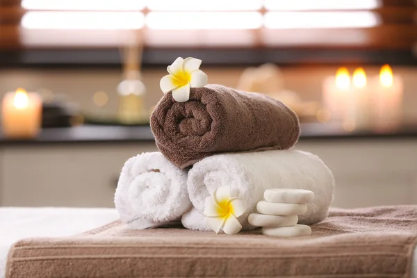 Kompozycja z ręcznikami, kwiatami i kamieniami na stole do masażu w salonie Spa — Zdjęcie stockowe