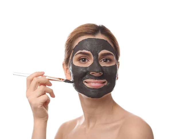 Beautiful woman applying black mask onto face against white background — Stock Photo, Image