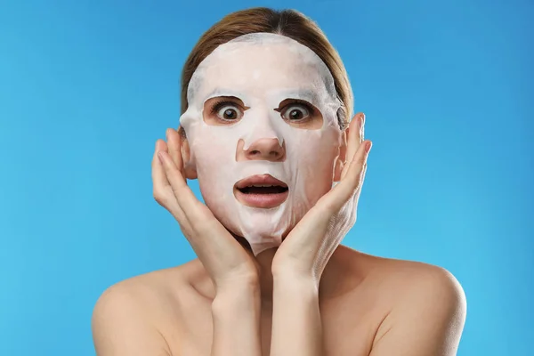 Emocjonalna kobieta z bawełnianym arkuszu maski na twarzy przed kolorowym tłem — Zdjęcie stockowe