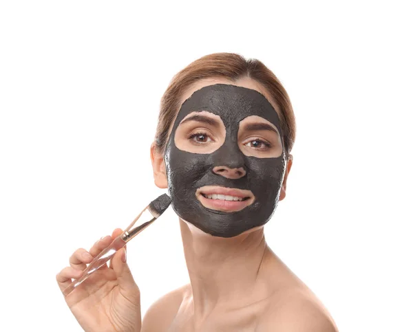 Beautiful woman applying black mask onto face against white background — Stock Photo, Image