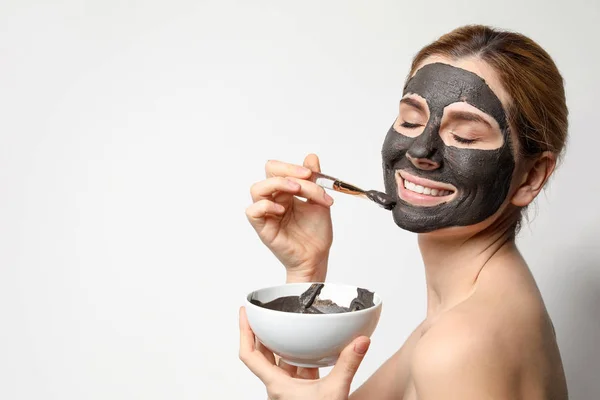 Piękna kobieta stosujące czarną maskę na twarz na jasnym tle. Miejsce na tekst — Zdjęcie stockowe